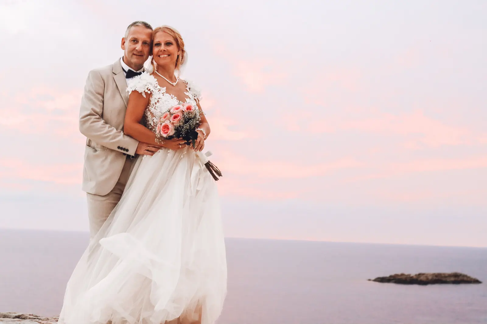 Newlyweds against a pastel sky by the sea